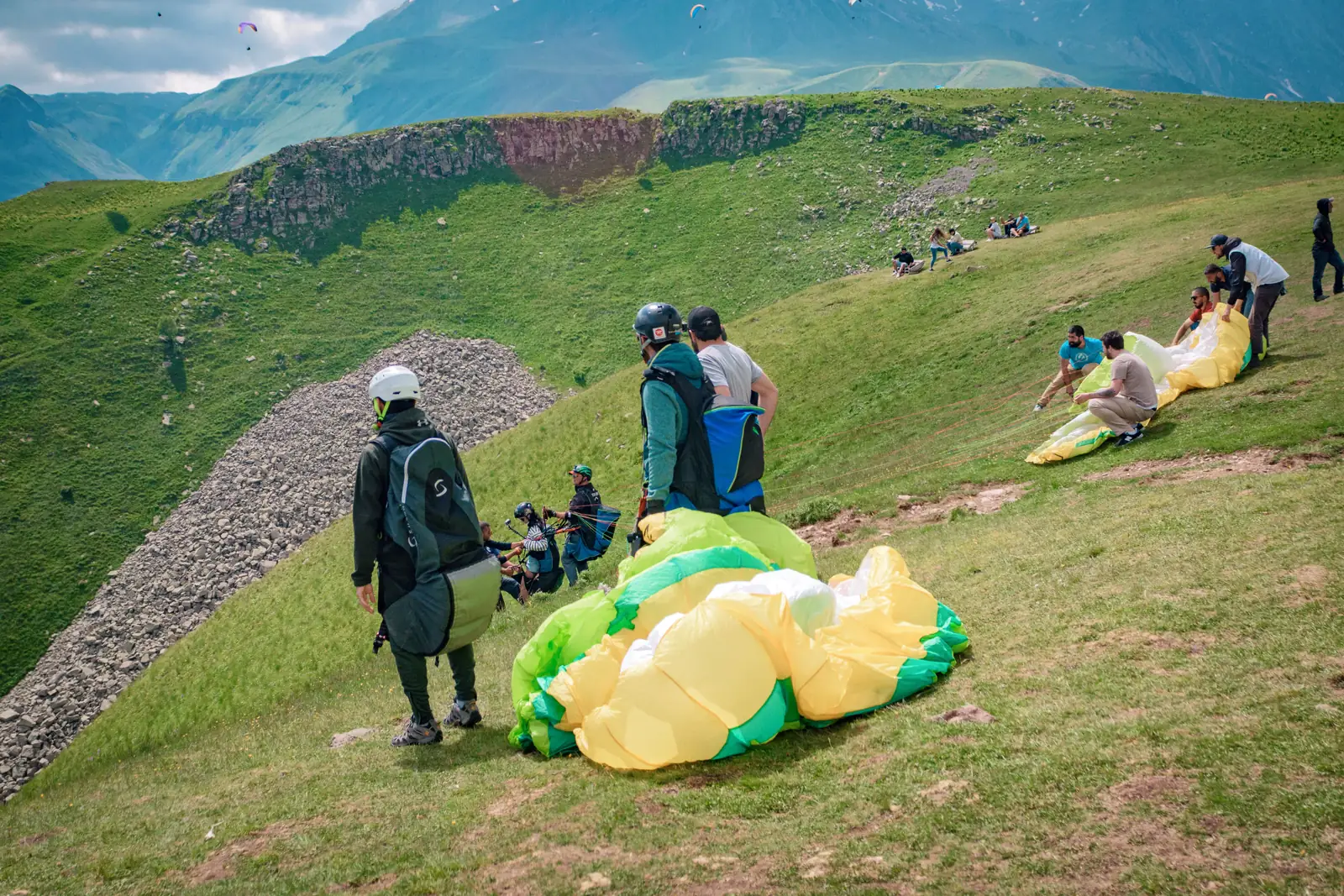 Pilots and passengers laying out their wings on the launch slope, valley behind