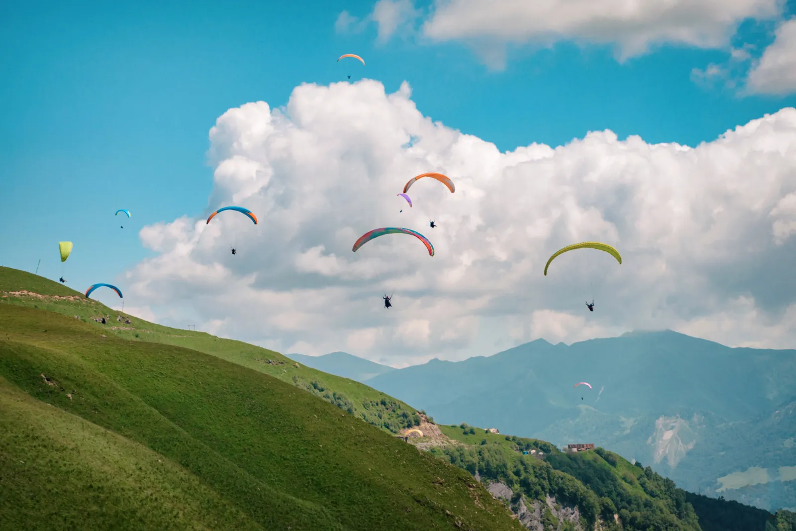 A dozen paragliders circling in the thermals above the green ridge at Gudauri