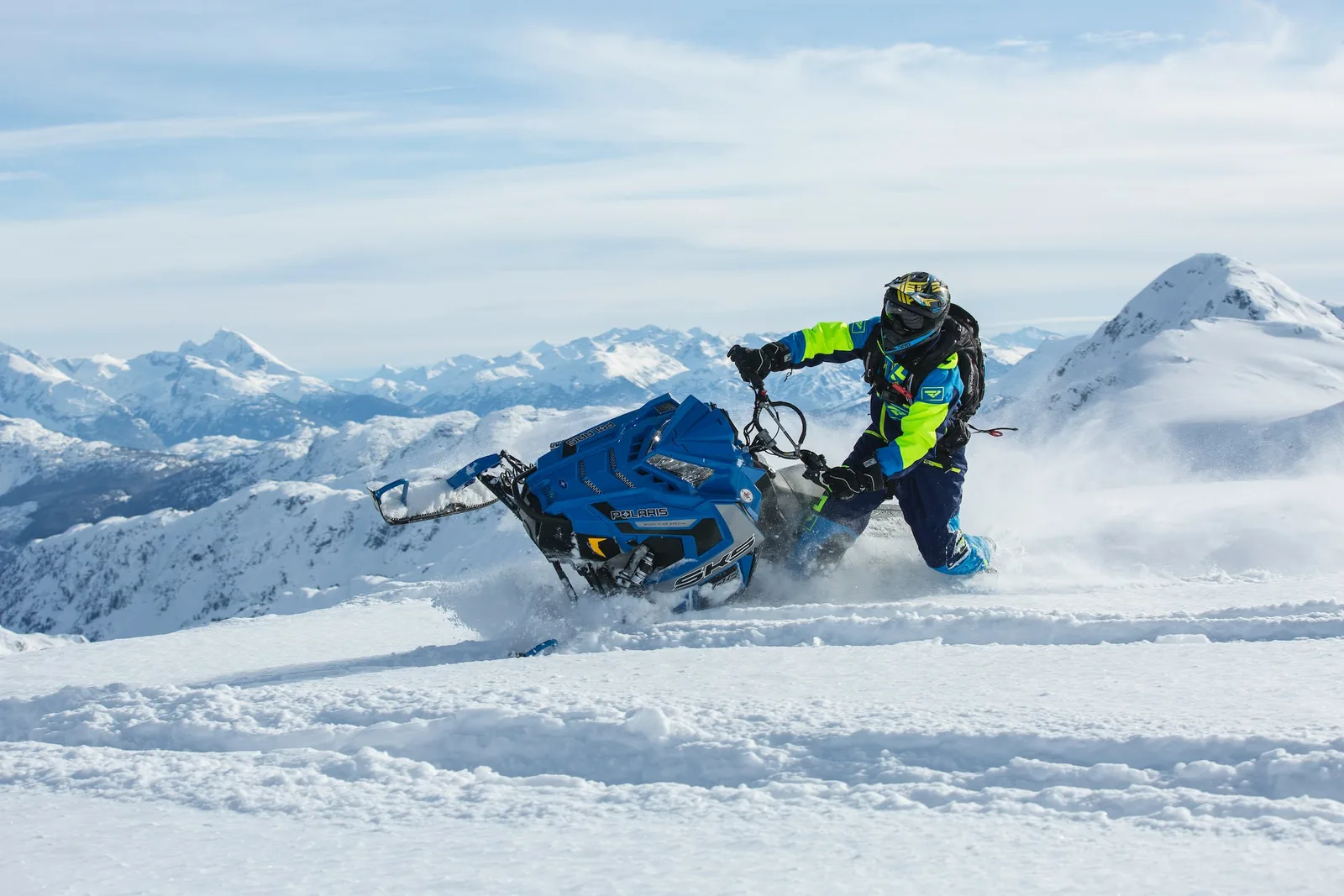 Rider leaning a snowmobile into a turn, spray flying, Caucasus peaks behind